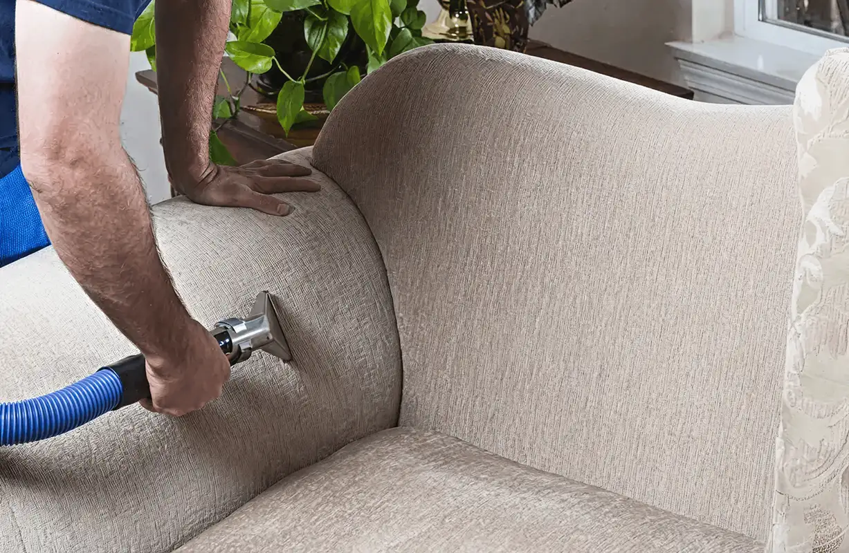 Professional upholstery cleaner deep-cleaning a fabric sofa with a handheld extraction tool and hose, Sarasota, FL.